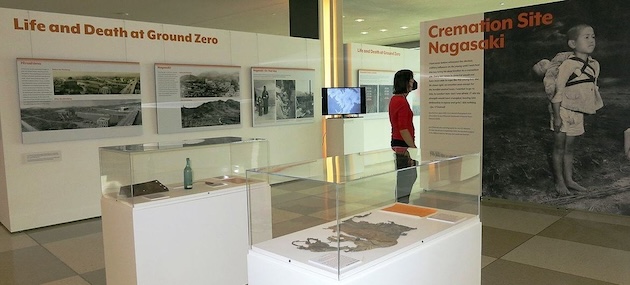 At a disarmament exhibition in UN Headquarters in New York, a visitor reads text about a young boy bringing his little brother to a cremation site in Nagasaki, Japan. Credit: UNODA/Erico Platt